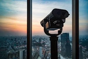 Public binoculars overlook a city during sunset.